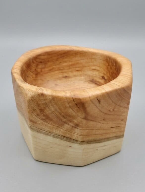 A faceted bowl turned across the sapwood line, where the wood changes color in a single stroke.